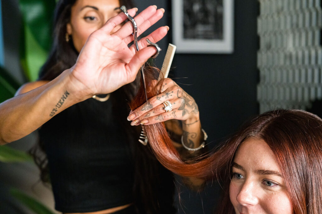 Tattooed hair stylist performing a precision shear cut in the dark-toned private suite at Verano Luxe salon near Austin Texas