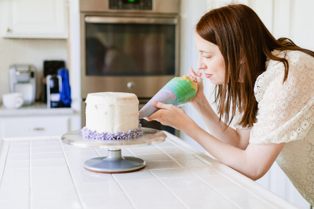 Woman decorating a cake on a cake stand with purple frosting