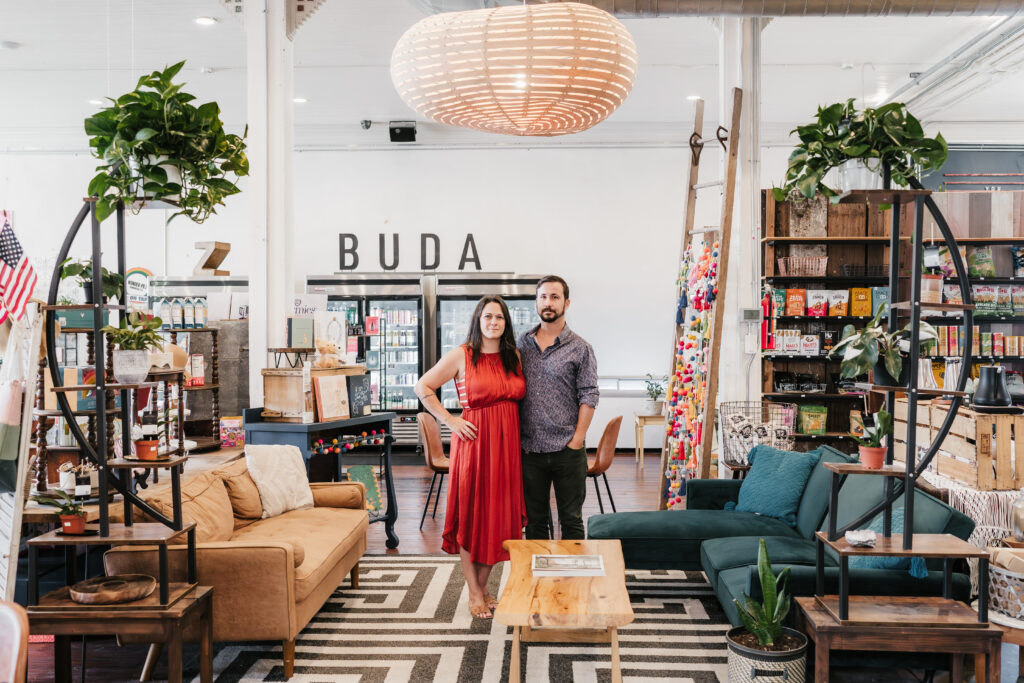 the owners of Zoi Market, Noa and Travis, standing in the center of the market, surrounded by couches, gift display tables and plants