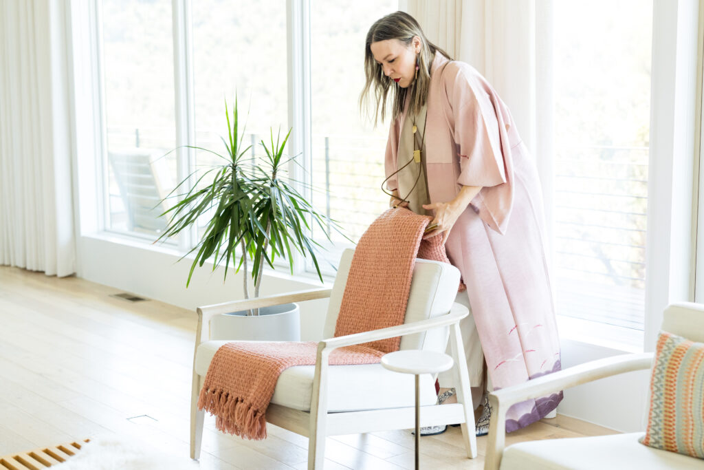 Woman in a long pink jacket fixing a blanket on the back of a chair